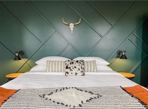 A bed with a patterned throw blanket next to a textured green wall with wooden side tables