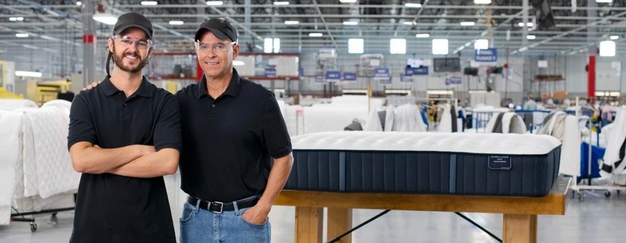 Father and son master craftsman standing in a Stearns & Foster factory in front of a newly completed mattress