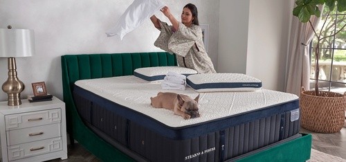 A woman putting pillow cases on while her dog naps on the bed